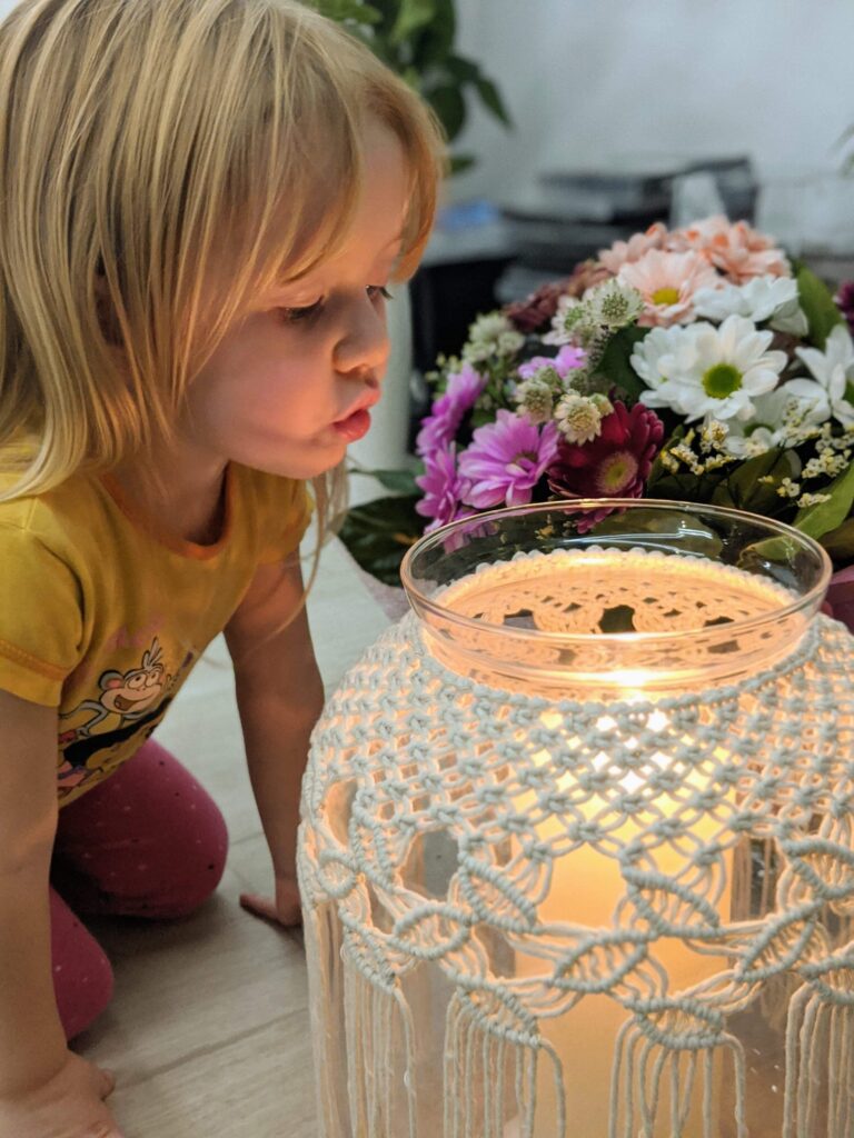 dziewczynka dmuchająca na świecę w lampionie ozdobionym makramą